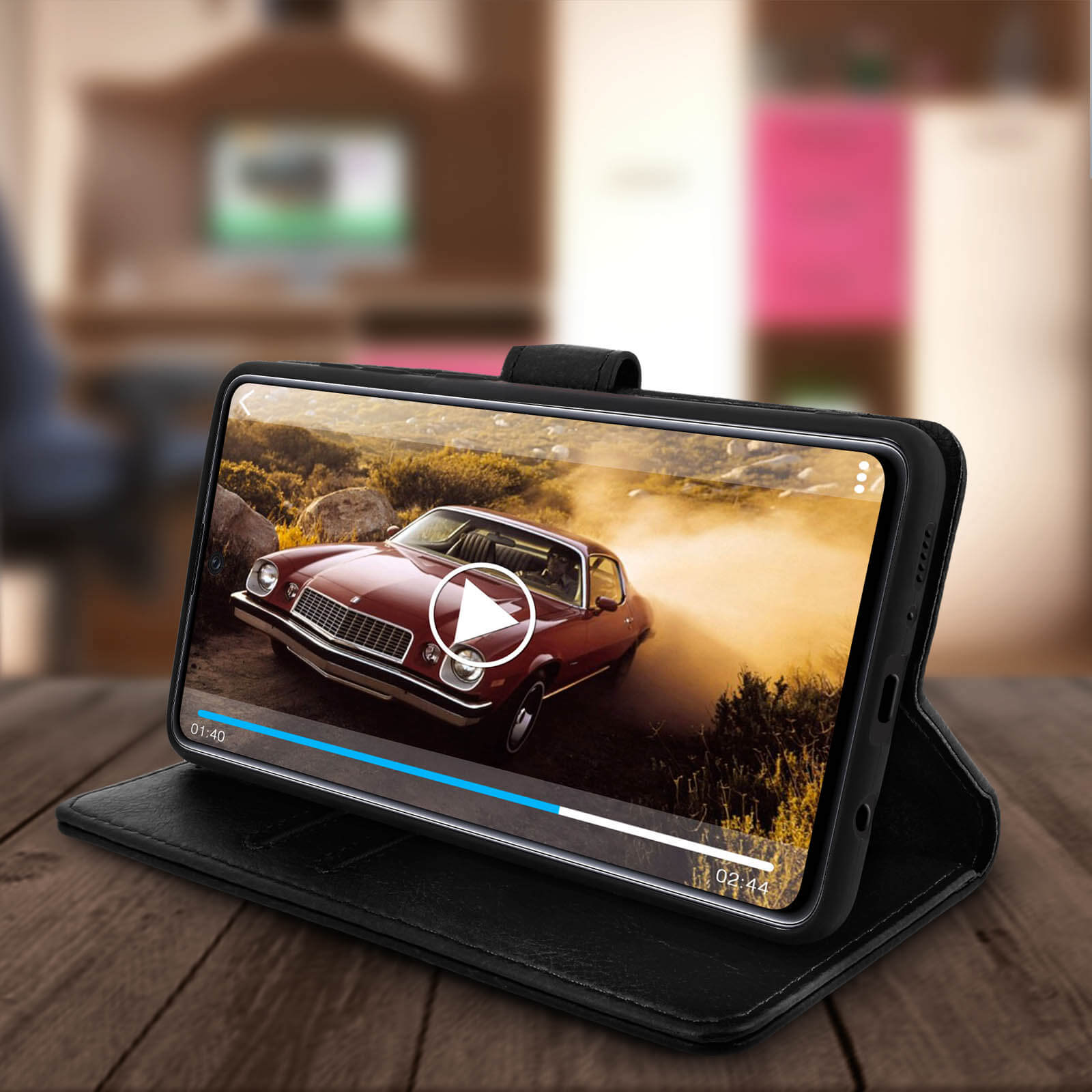 Telefono in custodia nera, mostra un film di auto su un tavolo di legno.