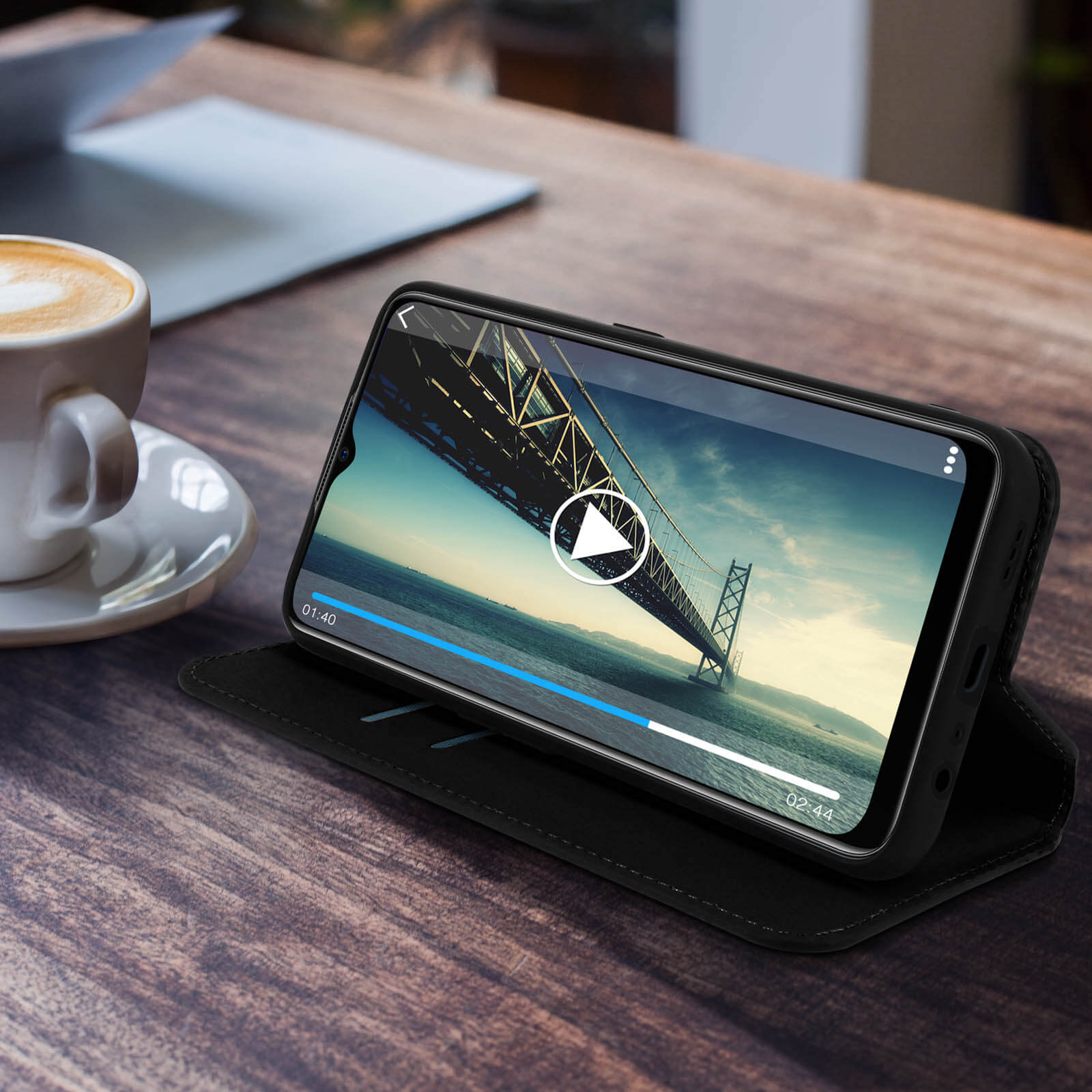 Telefoon op zwarte hoes, video afspelend, brug op achtergrond, houten tafel.