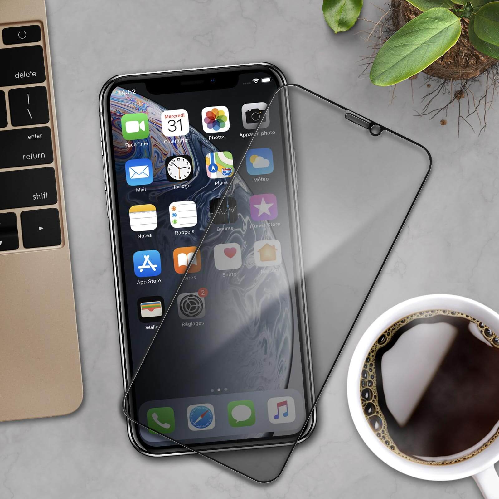 Un telefono con una protezione per lo schermo su una scrivania. La scrivania ha una tastiera, caffè e una pianta.