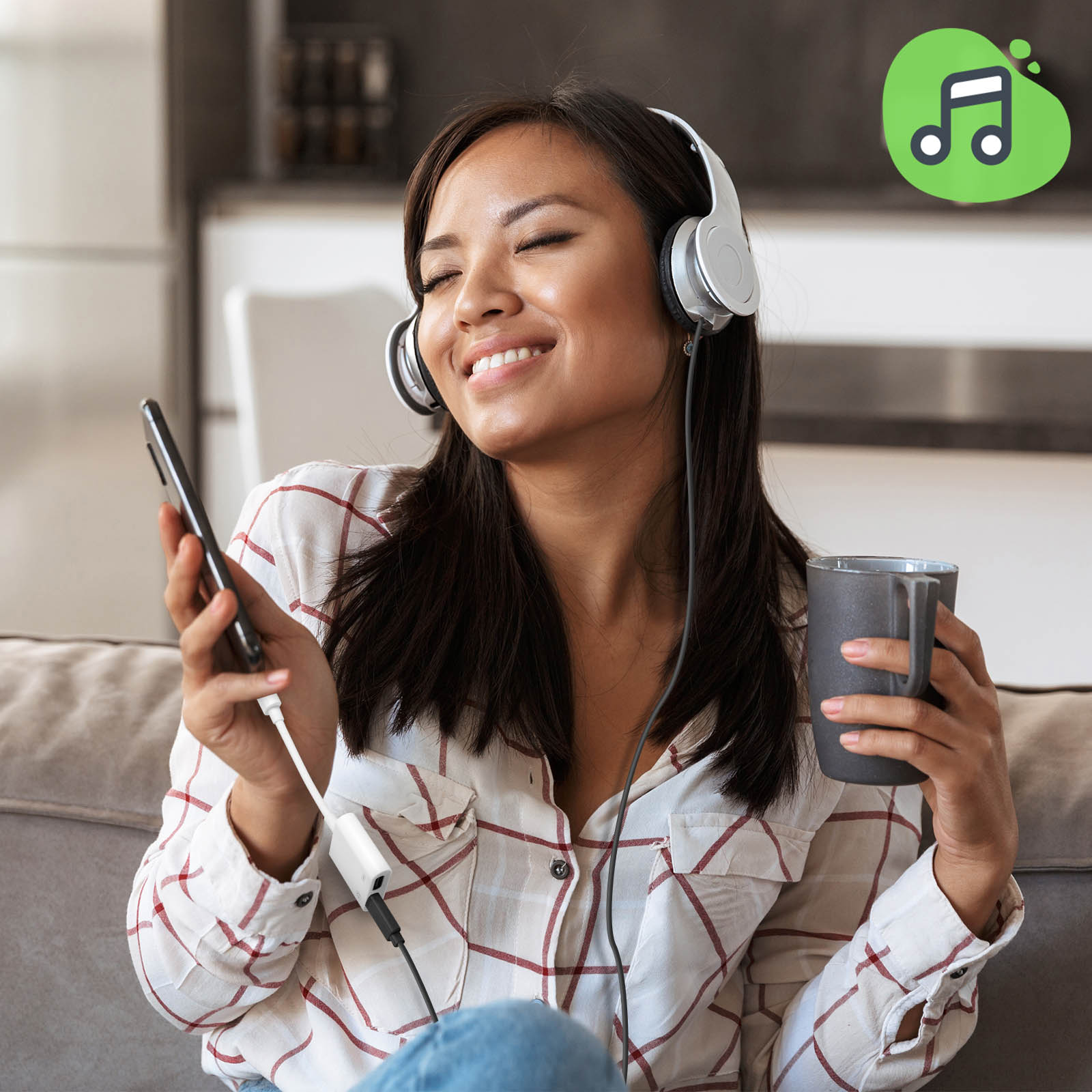 Donna sorridente, con le cuffie, che tiene un telefono e una tazza, con un logo di note musicali.