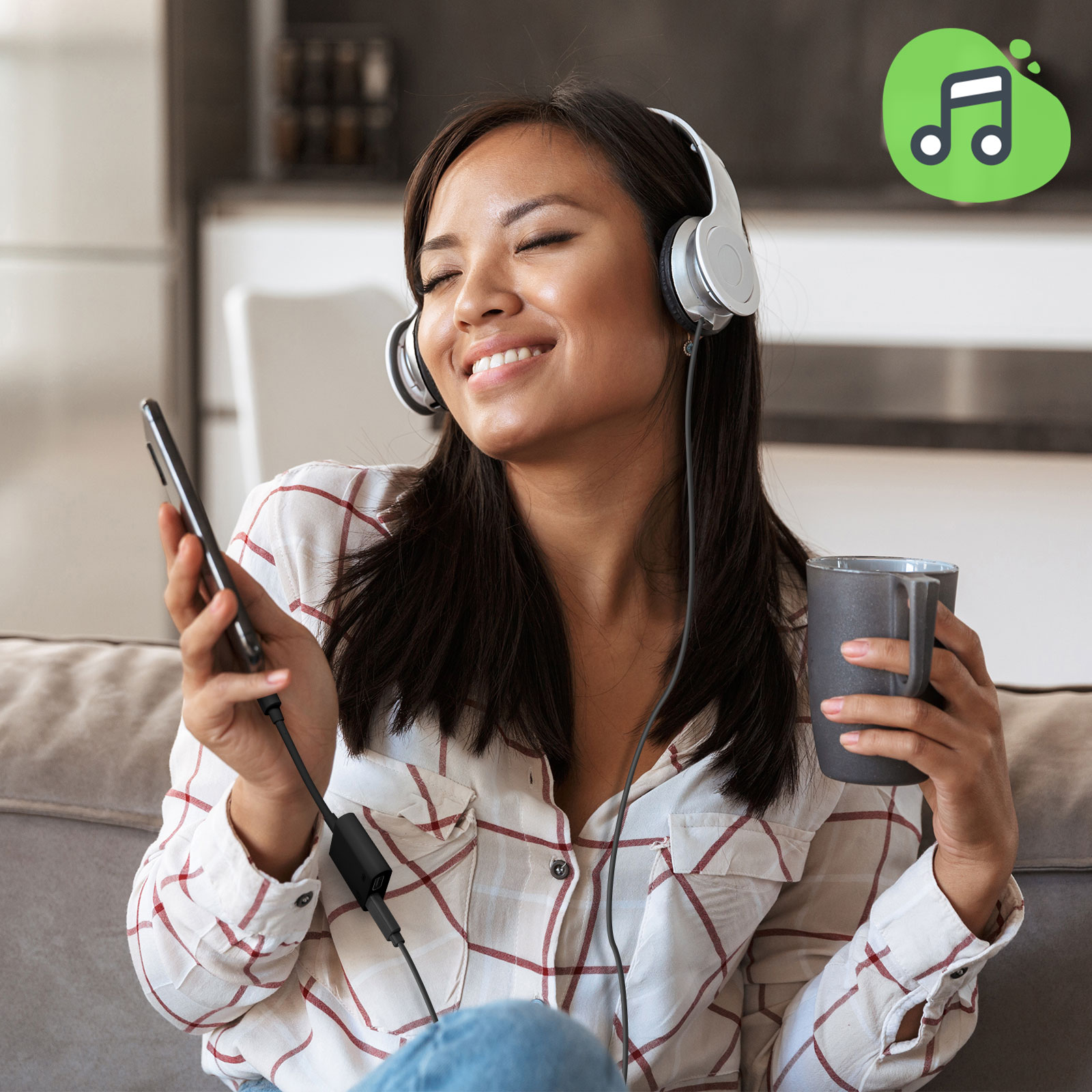 Donna con le cuffie, tiene un telefono e una tazza di caffè, sorride su un divano.