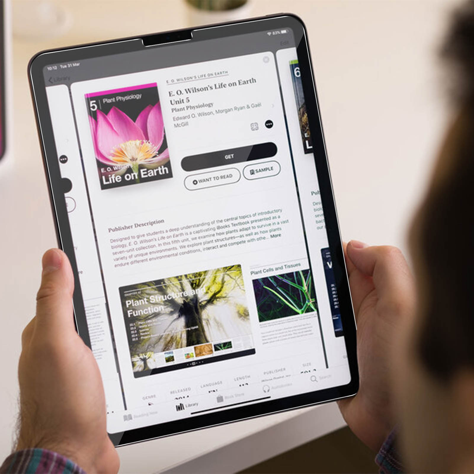 Persona che tiene in mano un tablet che mostra un ebook intitolato 'E.O. Wilson's Life on Earth'. La copertina del libro ha un fiore rosa.