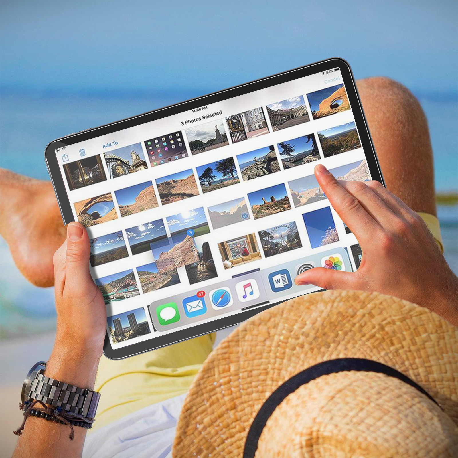 Persona sulla spiaggia con tablet con foto. Visibili cappello di paglia e orologio. Sfondo: mare e cielo blu.