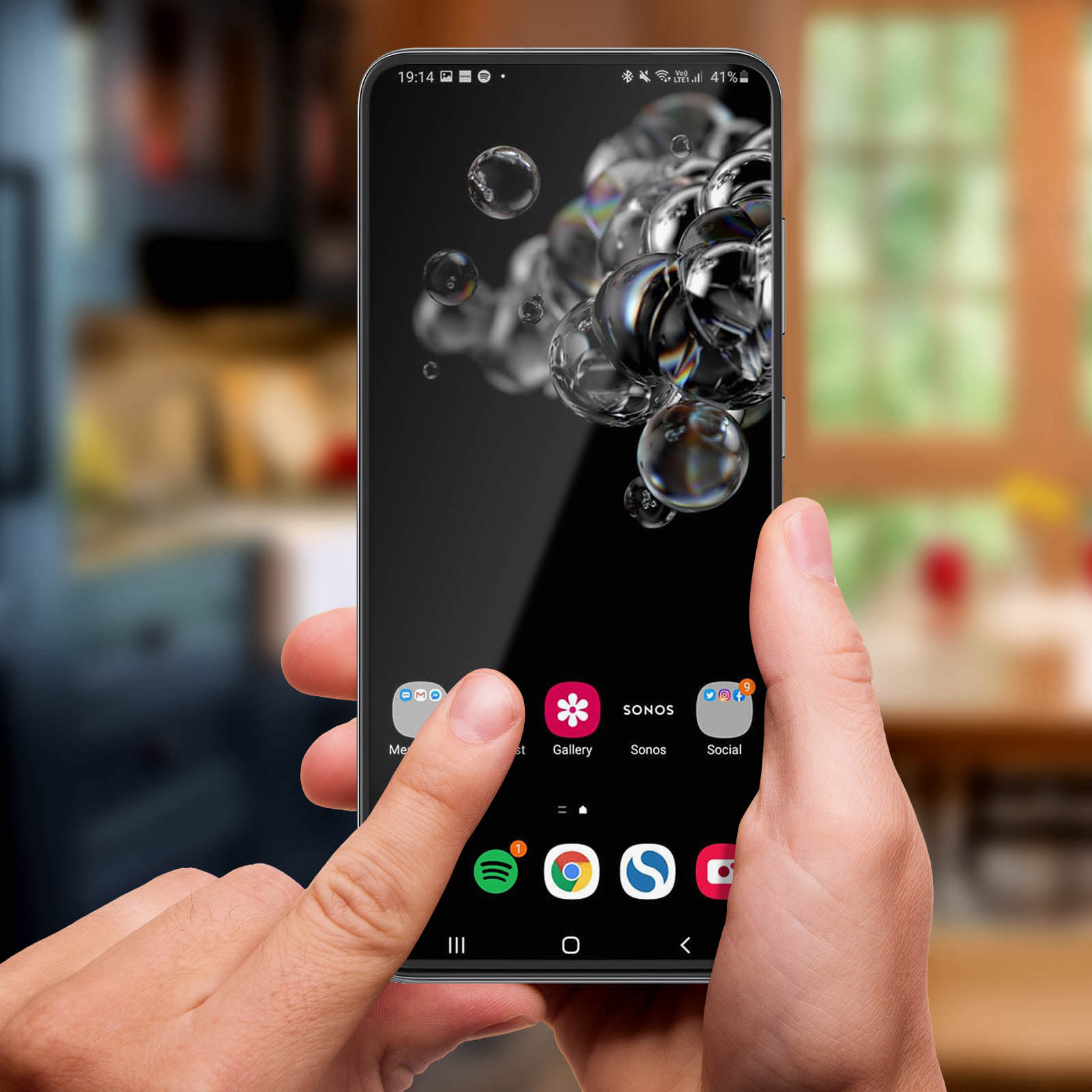 Una mano tiene in mano uno smartphone. Lo schermo mostra delle bolle. Le icone delle app sono visibili in basso. Lo sfondo è sfocato.