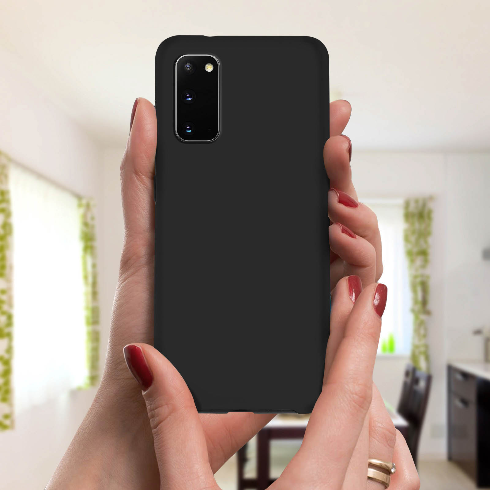 Zwarte telefoon vastgehouden door een persoon. Ze hebben rode nagellak. De achtergrond is een keuken.