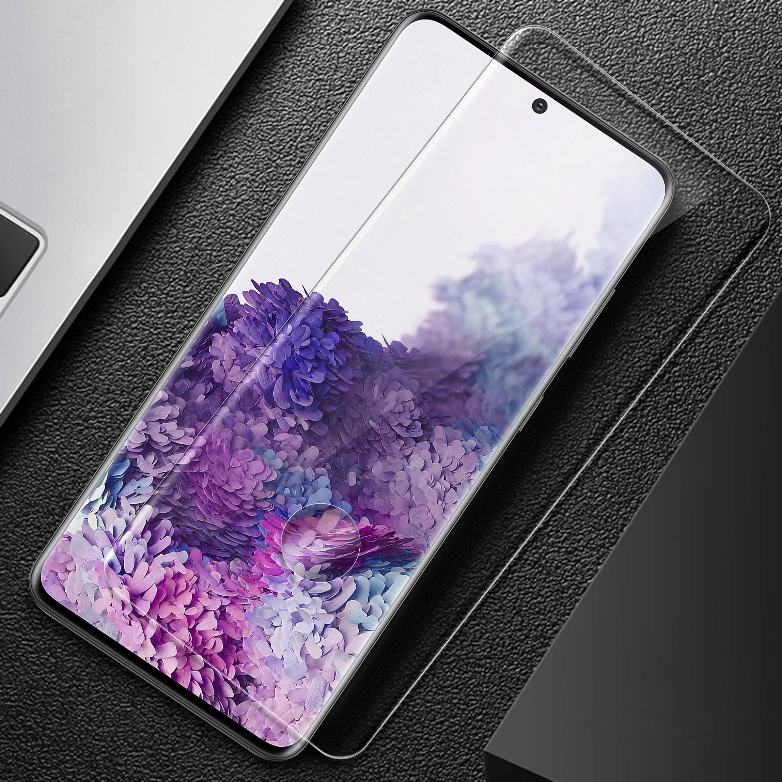 Telefono con protezione schermo, che mostra fiori, superficie nera e un laptop.