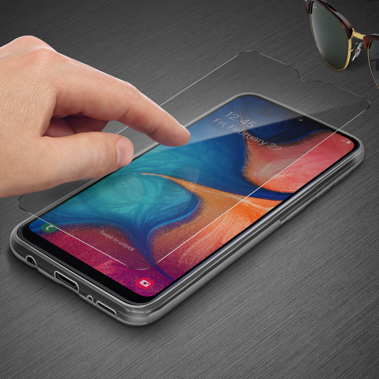 Mano che tocca la protezione dello schermo di un telefono, occhiali da sole sullo sfondo.