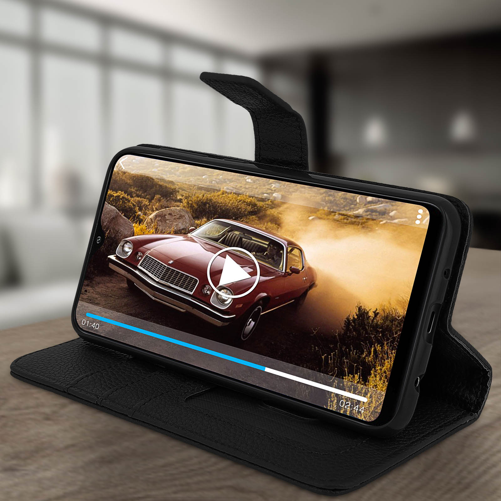 Téléphone dans un étui jouant une vidéo d'une voiture rouge. Étui noir sur une table en bois.