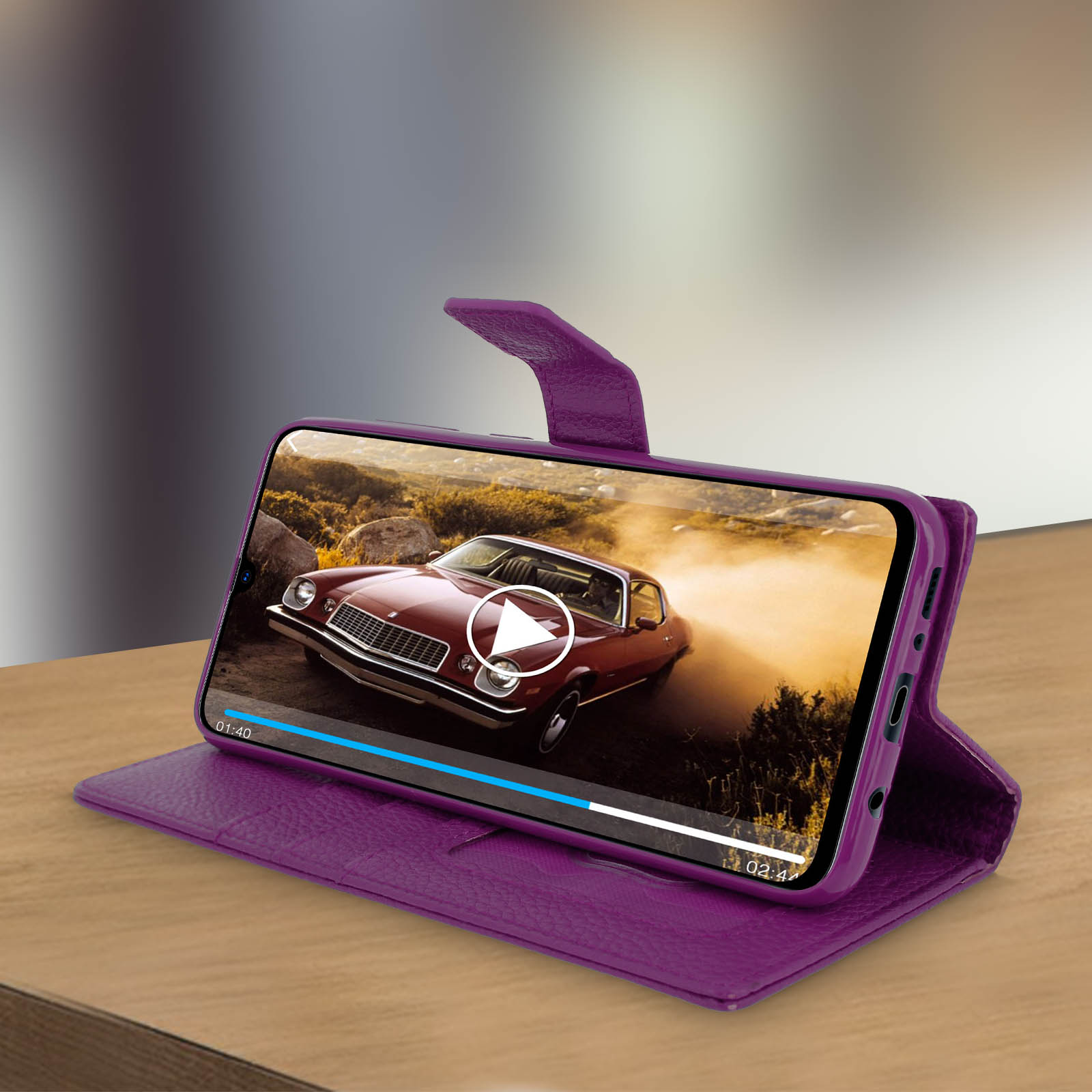 Un telefono in una custodia viola riproduce un video di un'auto. La scena è un'auto su una strada polverosa.