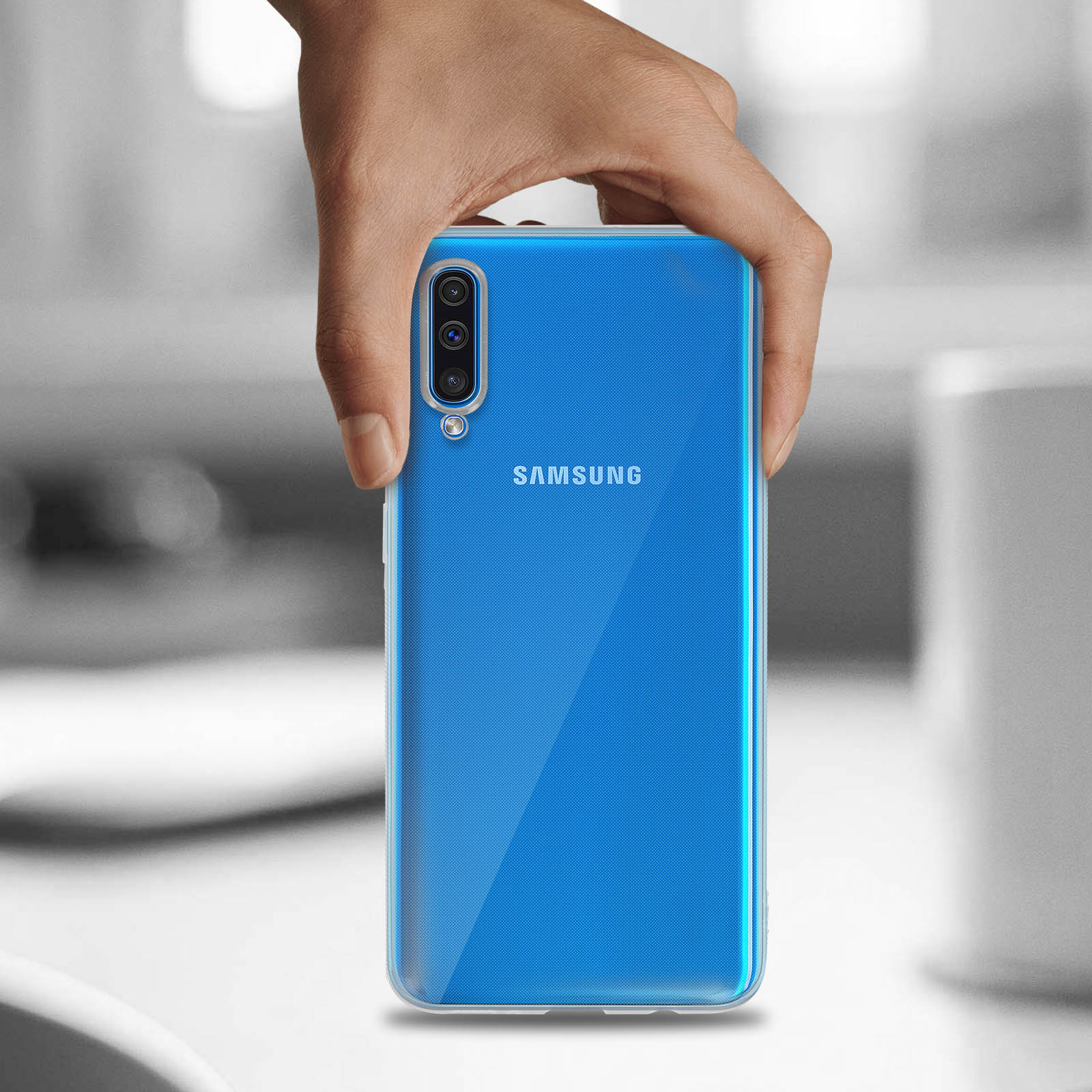 Hand hält ein klares blaues Telefon. Das Samsung-Logo ist sichtbar. Verschwommener Hintergrund.