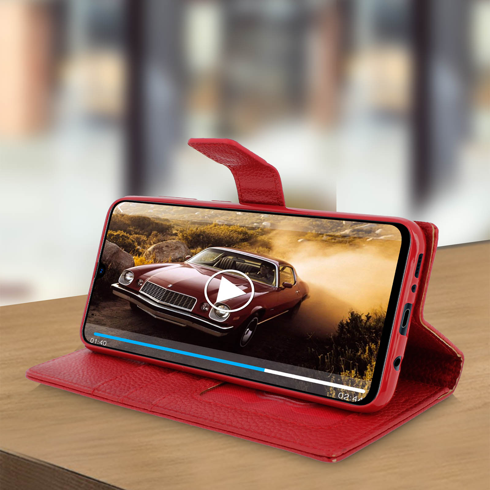 Étui de téléphone rouge avec un écran montrant une vidéo de voiture classique. Posé sur une table en bois.