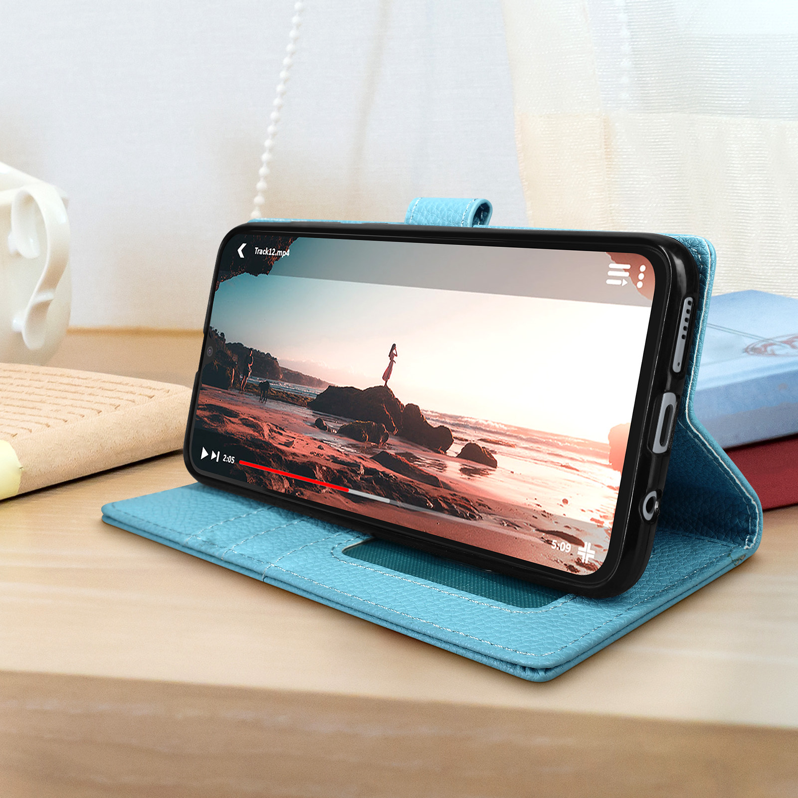 Un telefono in una custodia blu, che mostra un video, su un tavolo con libri.