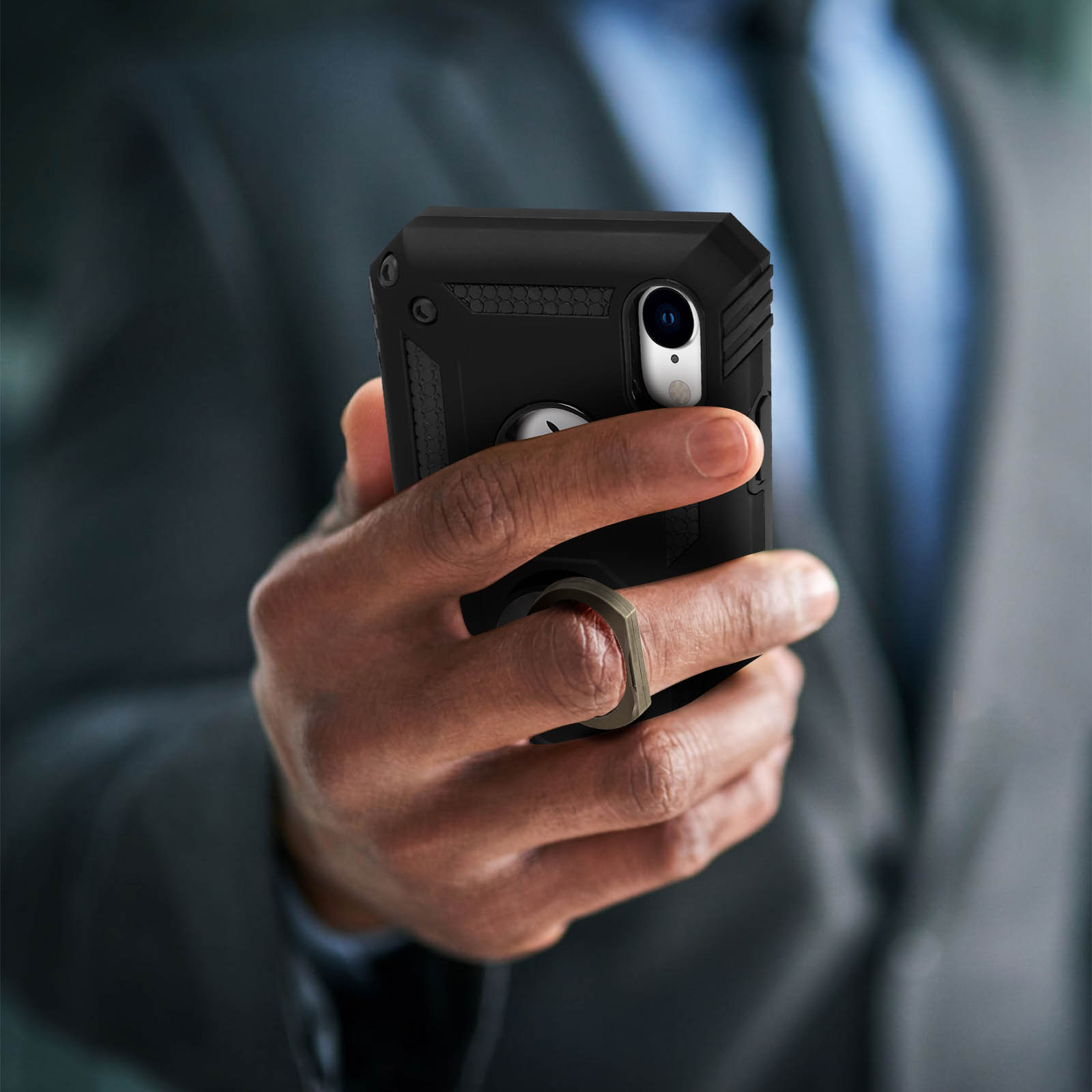 Hand met een zwarte telefoon met een ringhouder, tegen een vage achtergrond van een pak.