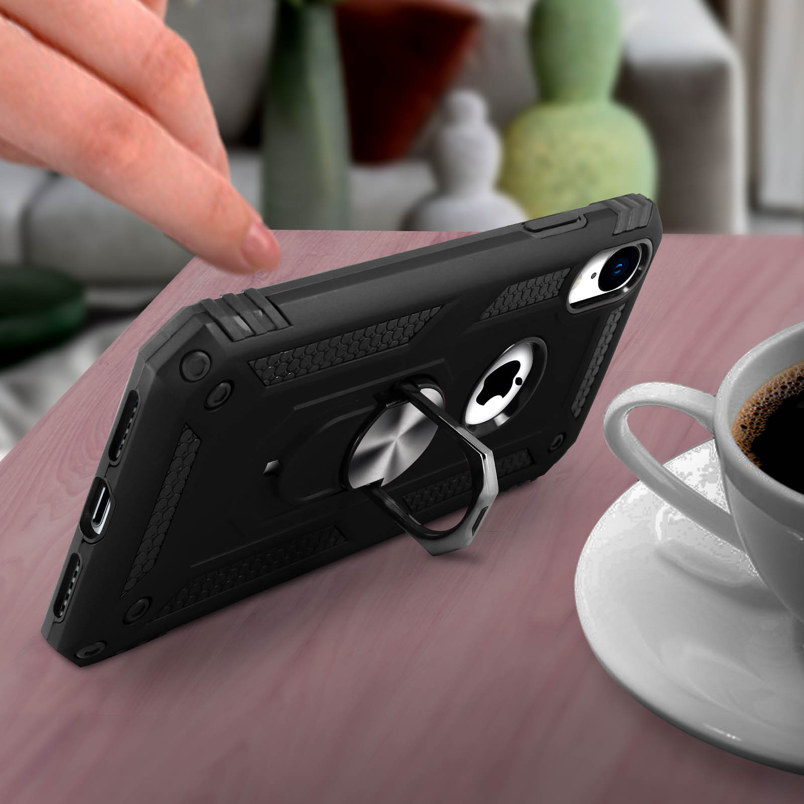 Zwarte telefoonhoes met een ringstandaard op een houten tafel, met een kopje koffie.