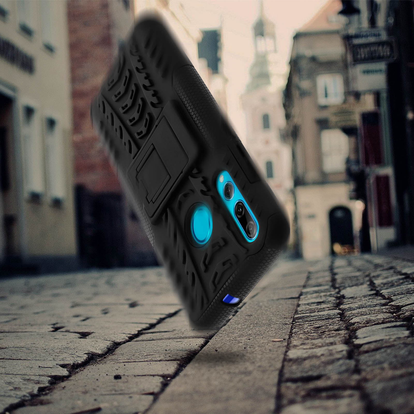 Coque de téléphone noire avec un support sur une rue pavée, arrière-plan flou.