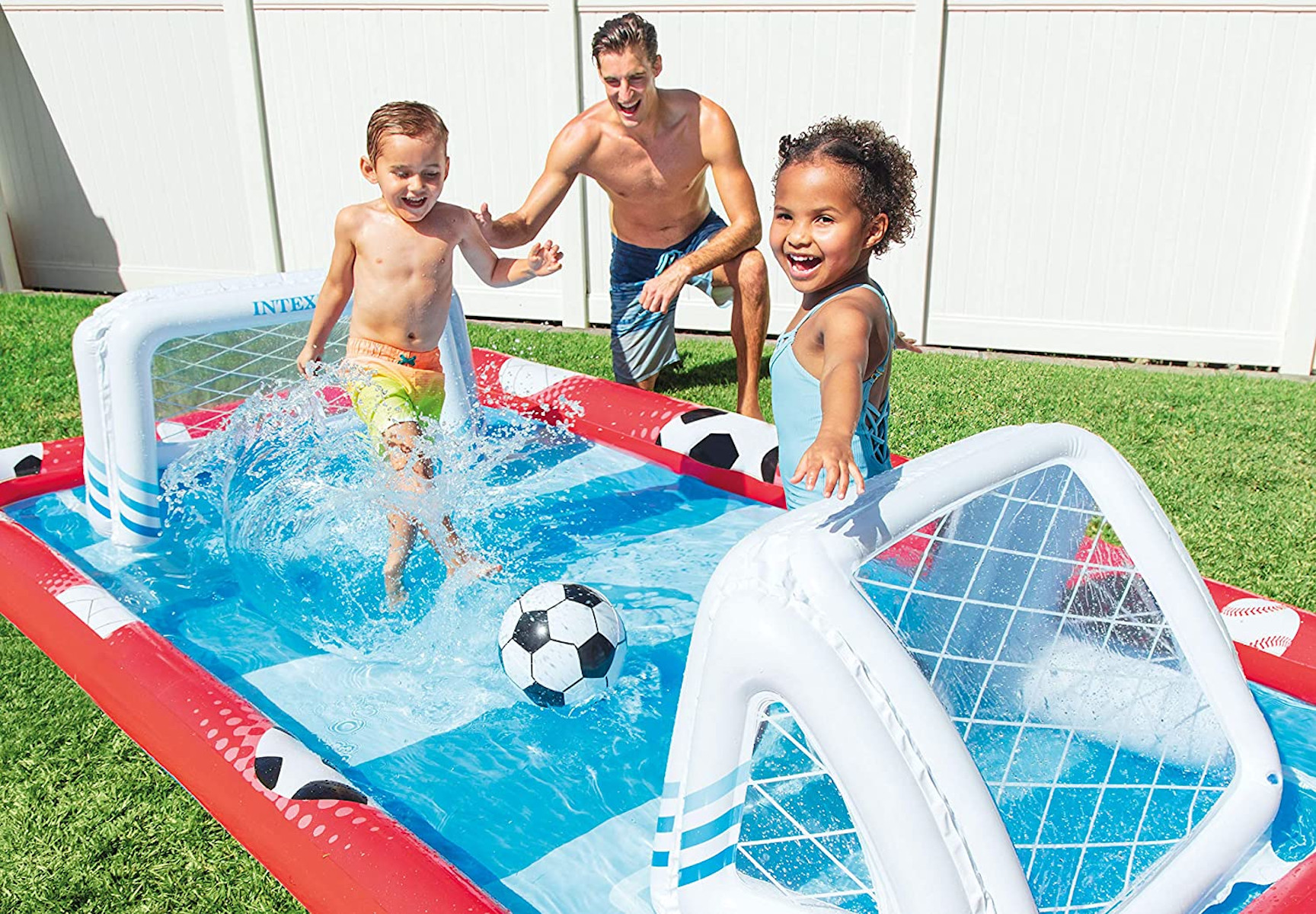 Bambini giocano a calcio in piscina con un uomo. Porte rosse e bianche.