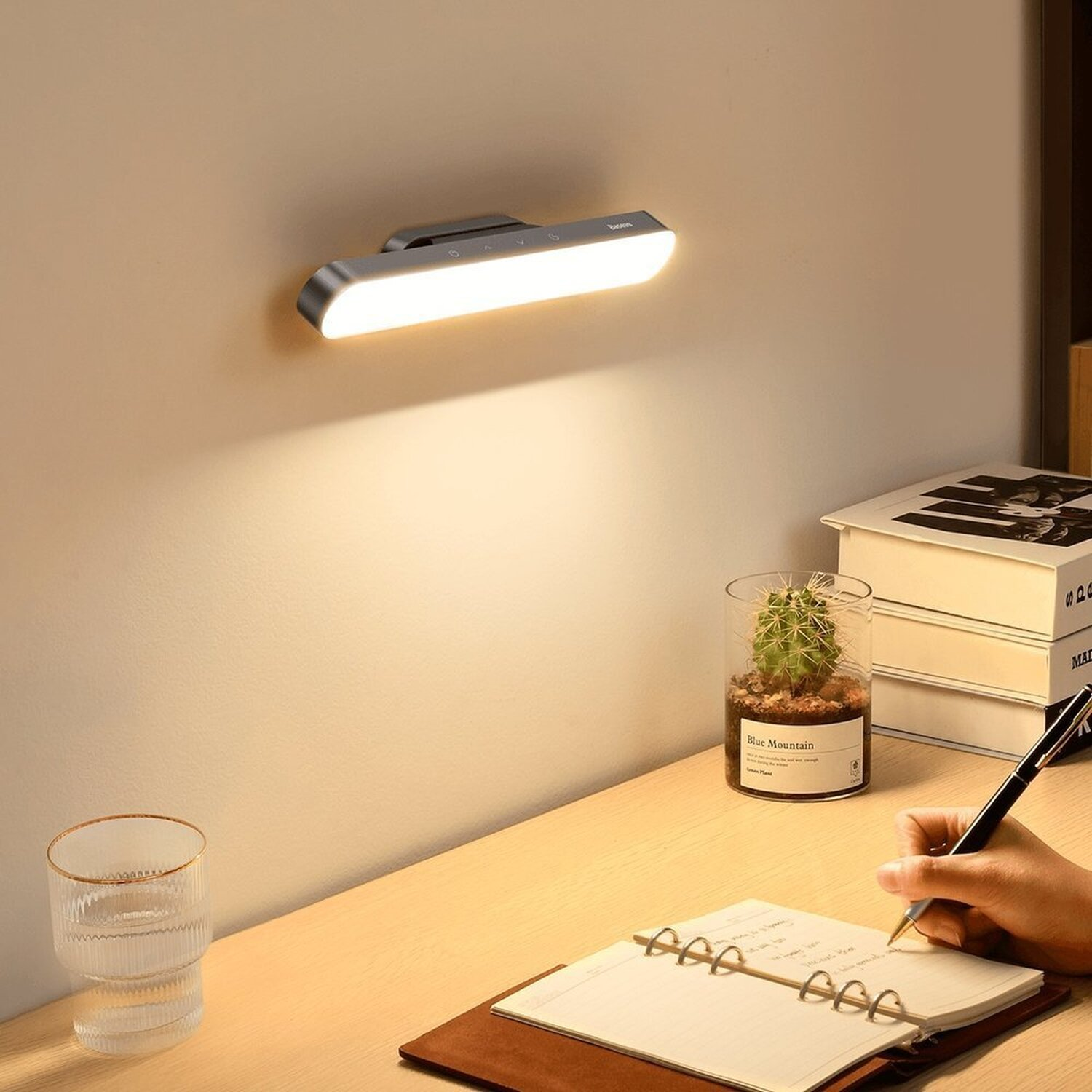 Bureaublad met een lamp aan de muur, cactus, boeken en een persoon die schrijft.