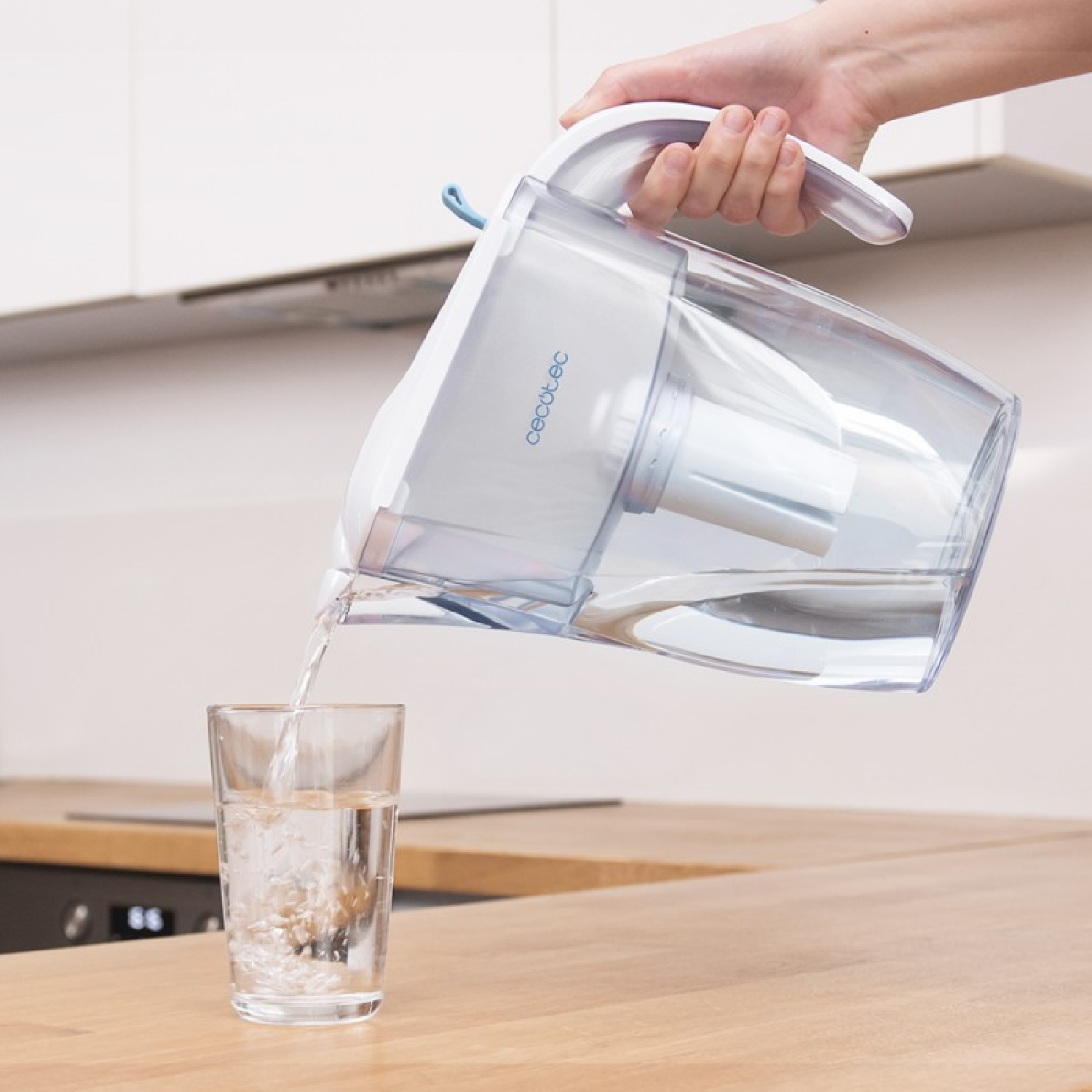 Una persona versa acqua da un filtro per acqua bianco e blu in un bicchiere.