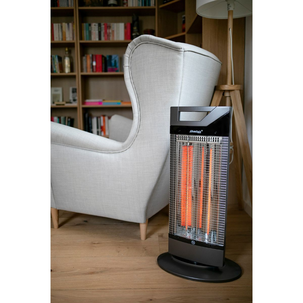Ein schwarzer Heizstrahler mit leuchtenden orangefarbenen Elementen, neben einem weißen Sessel.