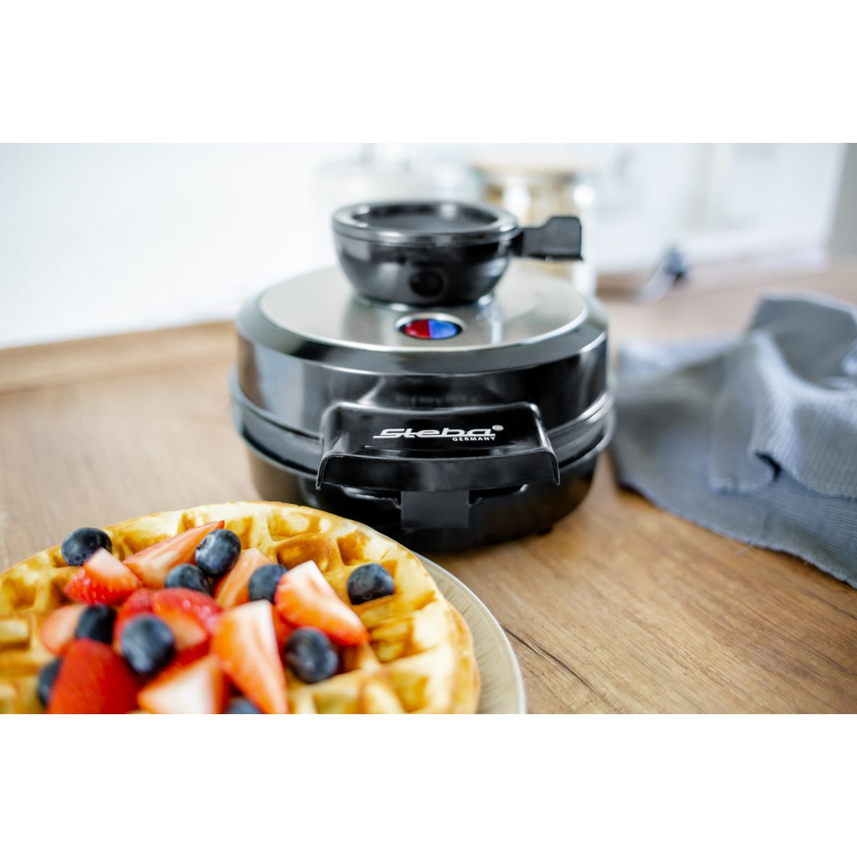 Waffeleisen mit Waffel, Erdbeeren und Blaubeeren auf einem Teller.