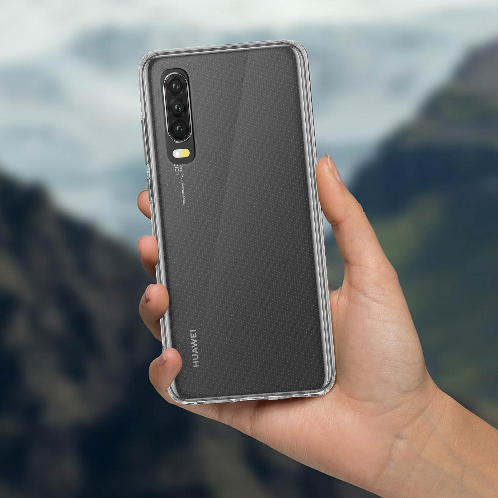 Mano che tiene telefono con custodia trasparente; sfondo sfocato di montagne.
