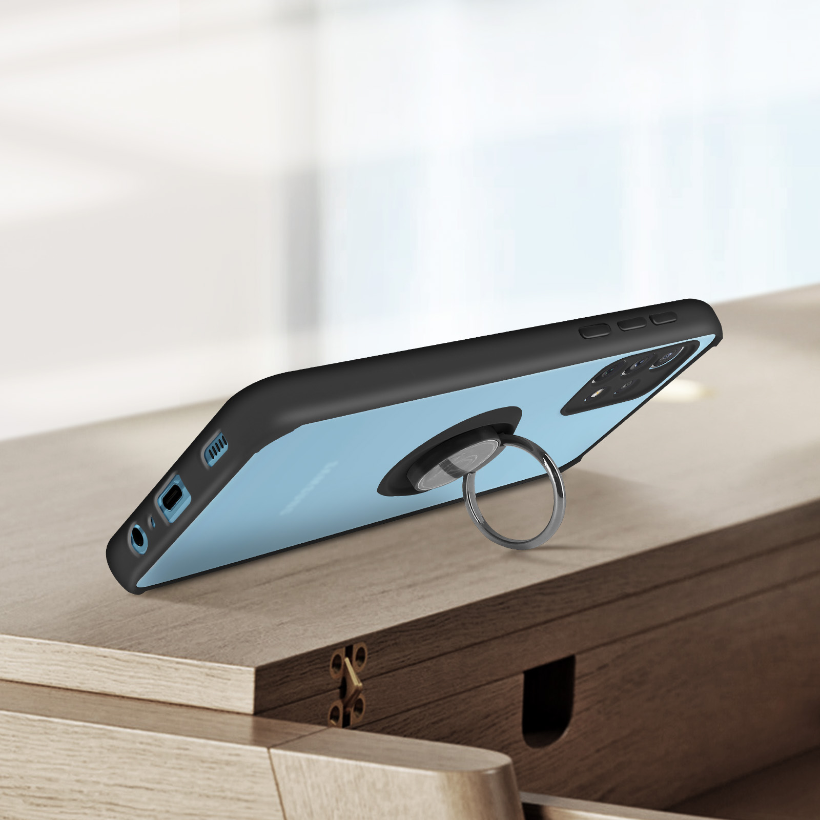 Un téléphone noir avec un support en anneau sur une table en bois, avec une fenêtre derrière.