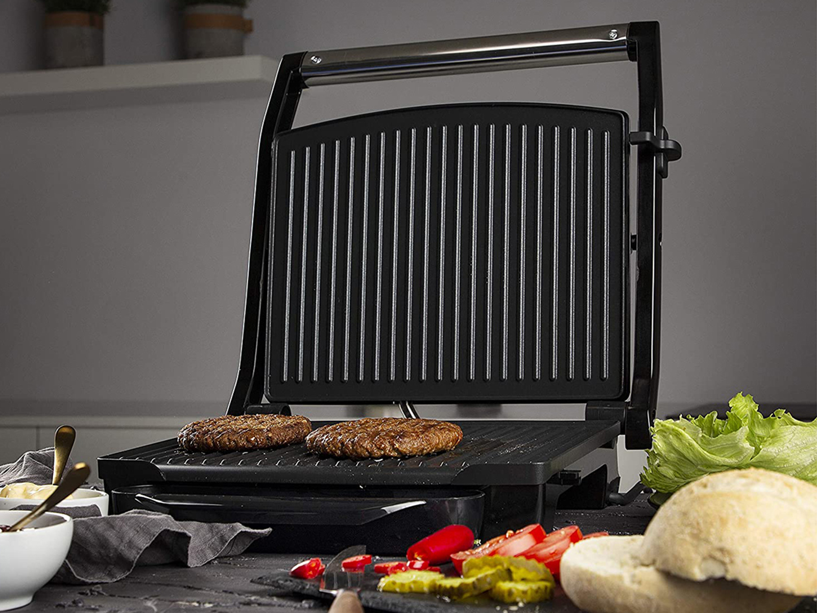 Schwarzer Grill mit zwei bratenen Burgern, mit Beilagen wie Salat und Tomaten.