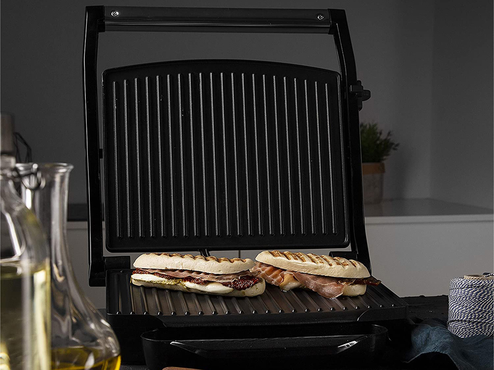 Sandwiches in einem schwarzen Panini-Grill, mit Öl und Bindfaden im Hintergrund.