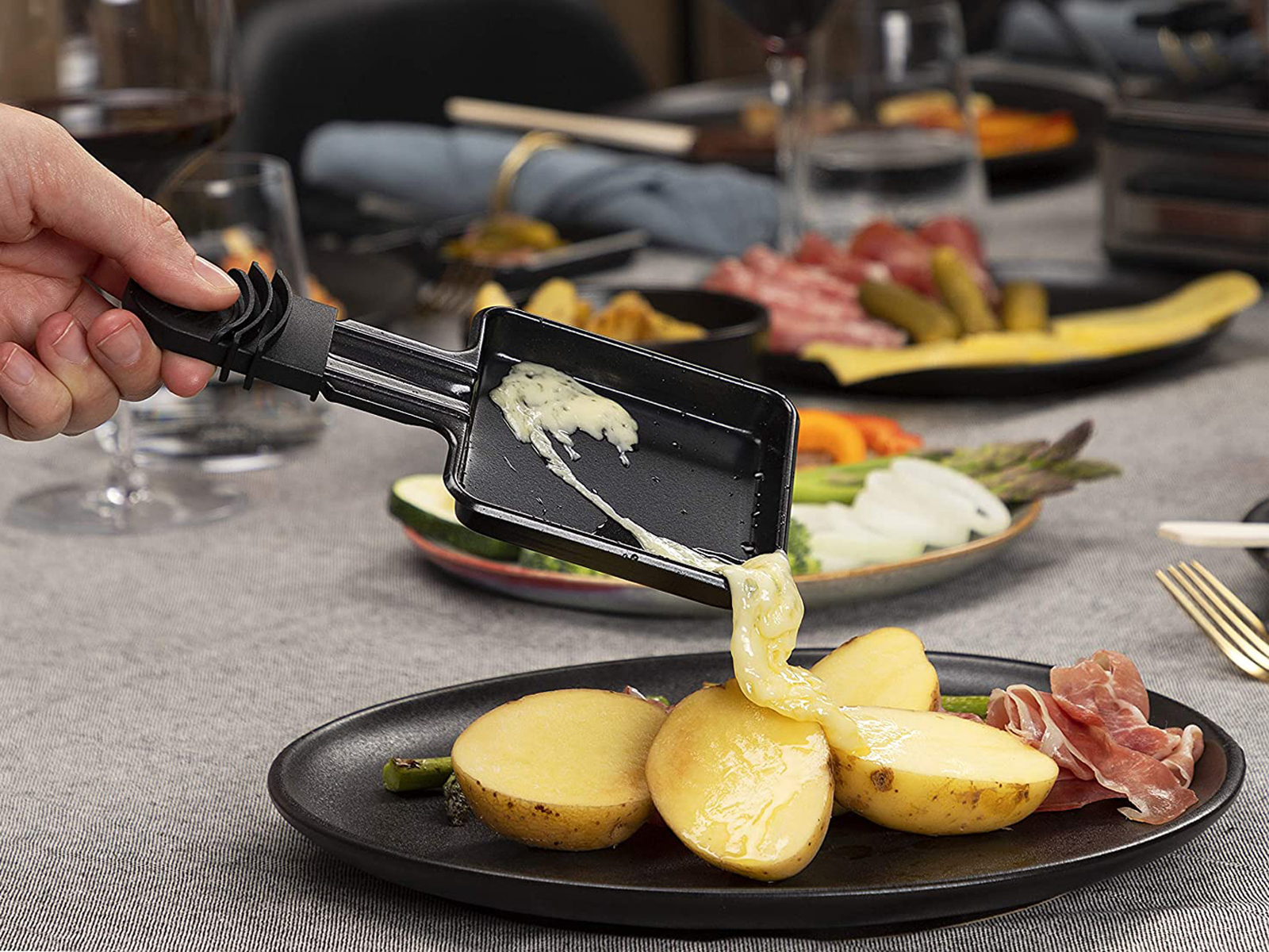 Osoba roztapiająca ser na ziemniakach. Pokrojone ziemniaki, mięso i warzywa na talerzu.