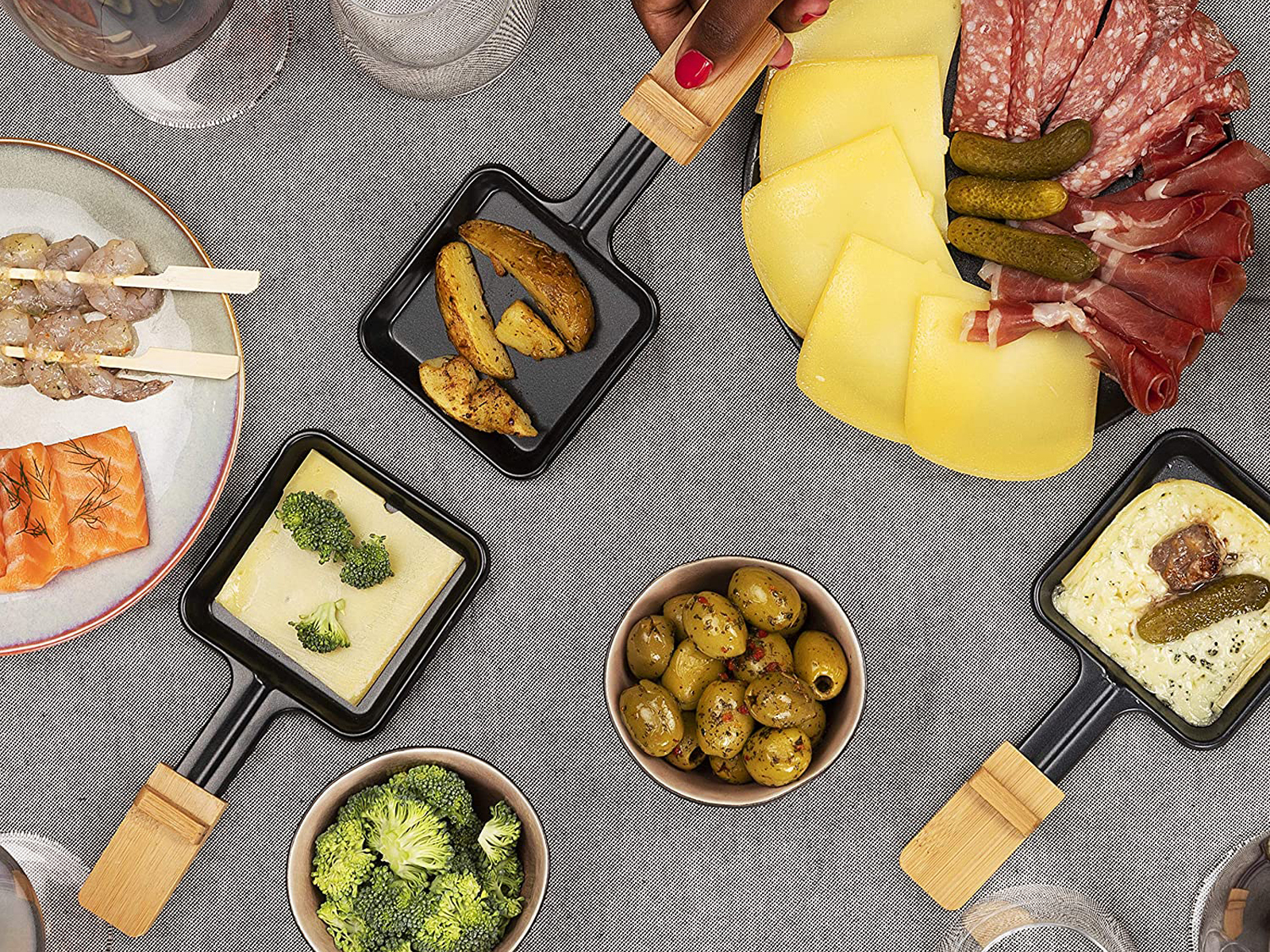 Posiłek raclette z serem, ziemniakami i mięsem, oliwkami i brokułami na stole.