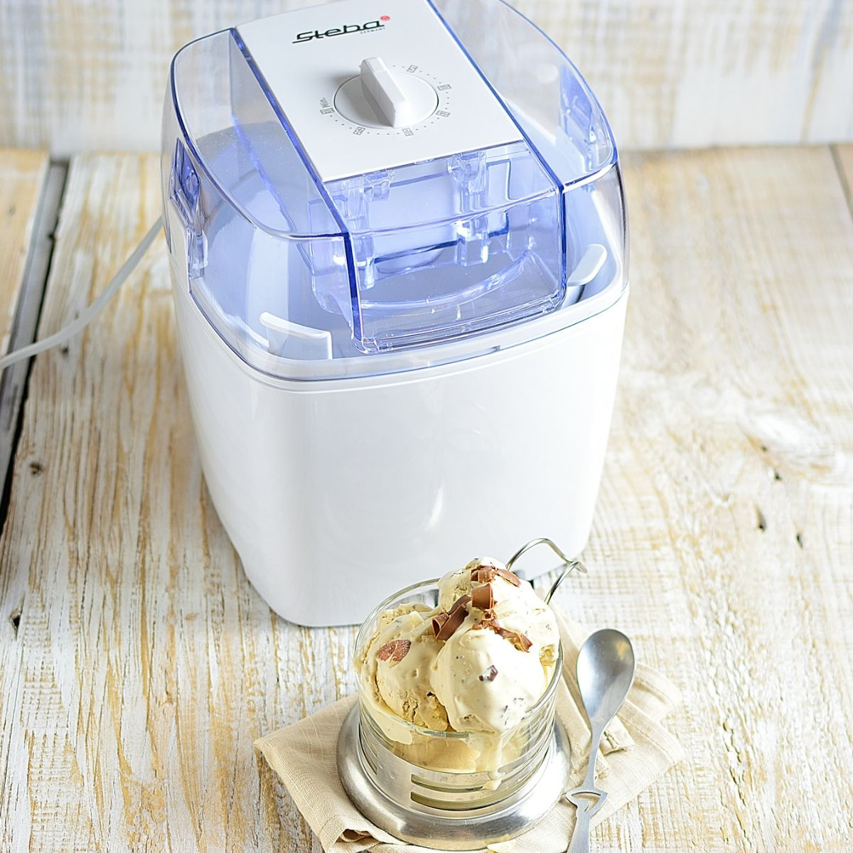 Gelatiera con gelato in un bicchiere. Tavolo di legno. Elettrodomestico bianco con dettagli blu.