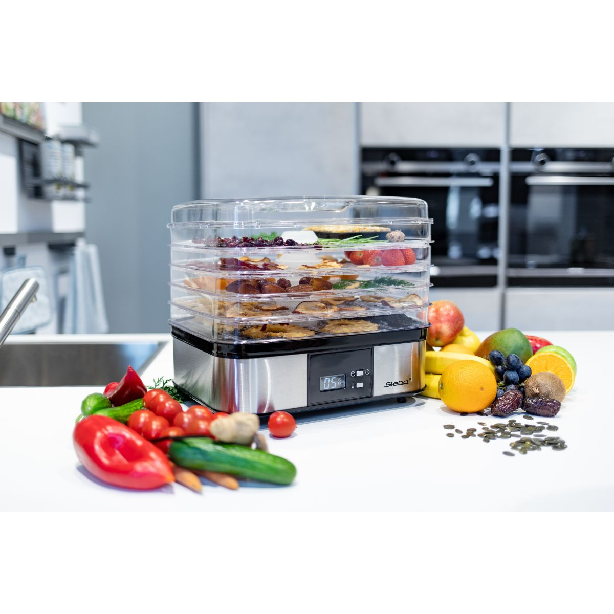 Lebensmitteltrockner mit getrocknetem Obst und Gemüse. Silber und schwarz. Weiße Arbeitsplatte und Küche.