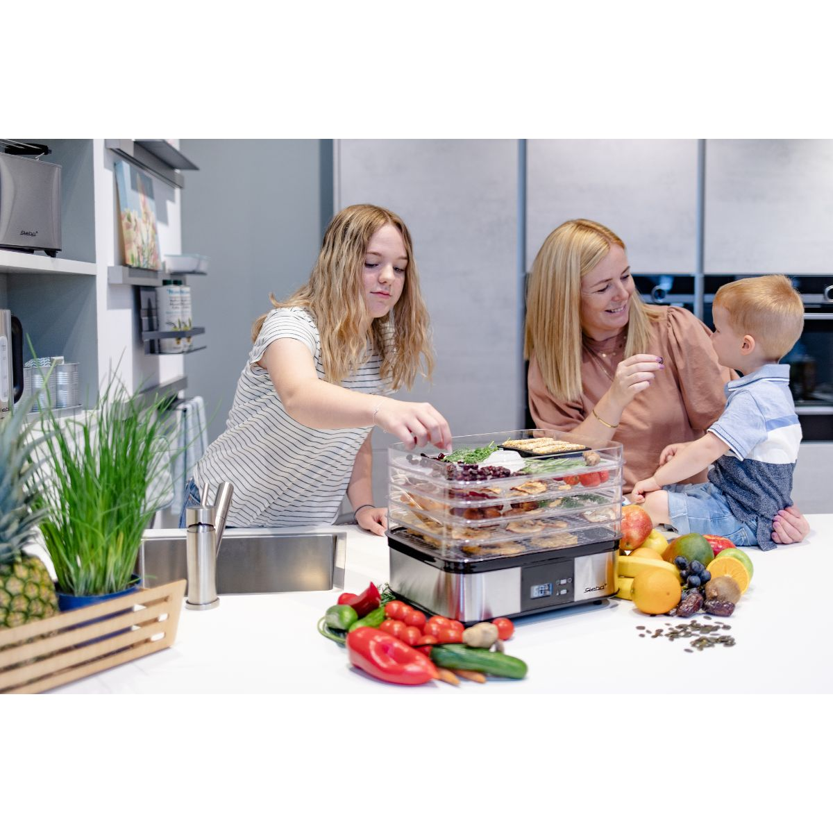 Eine Familie benutzt einen Dörrautomaten. Verschiedene Früchte und Gemüse befinden sich auf den Tabletts.