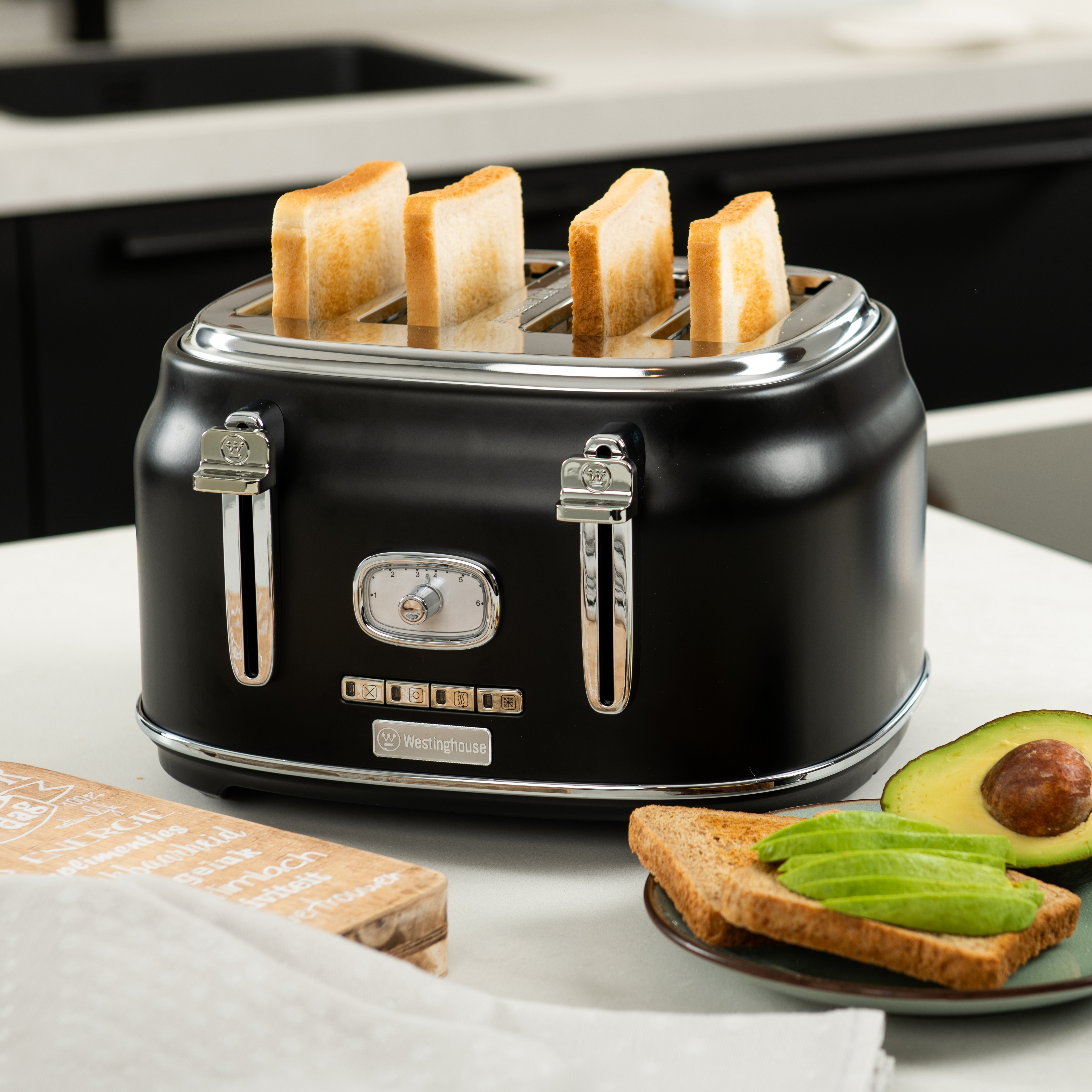 Schwarzer Toaster mit vier Toastscheiben, plus Schneidebrett und Avocado.