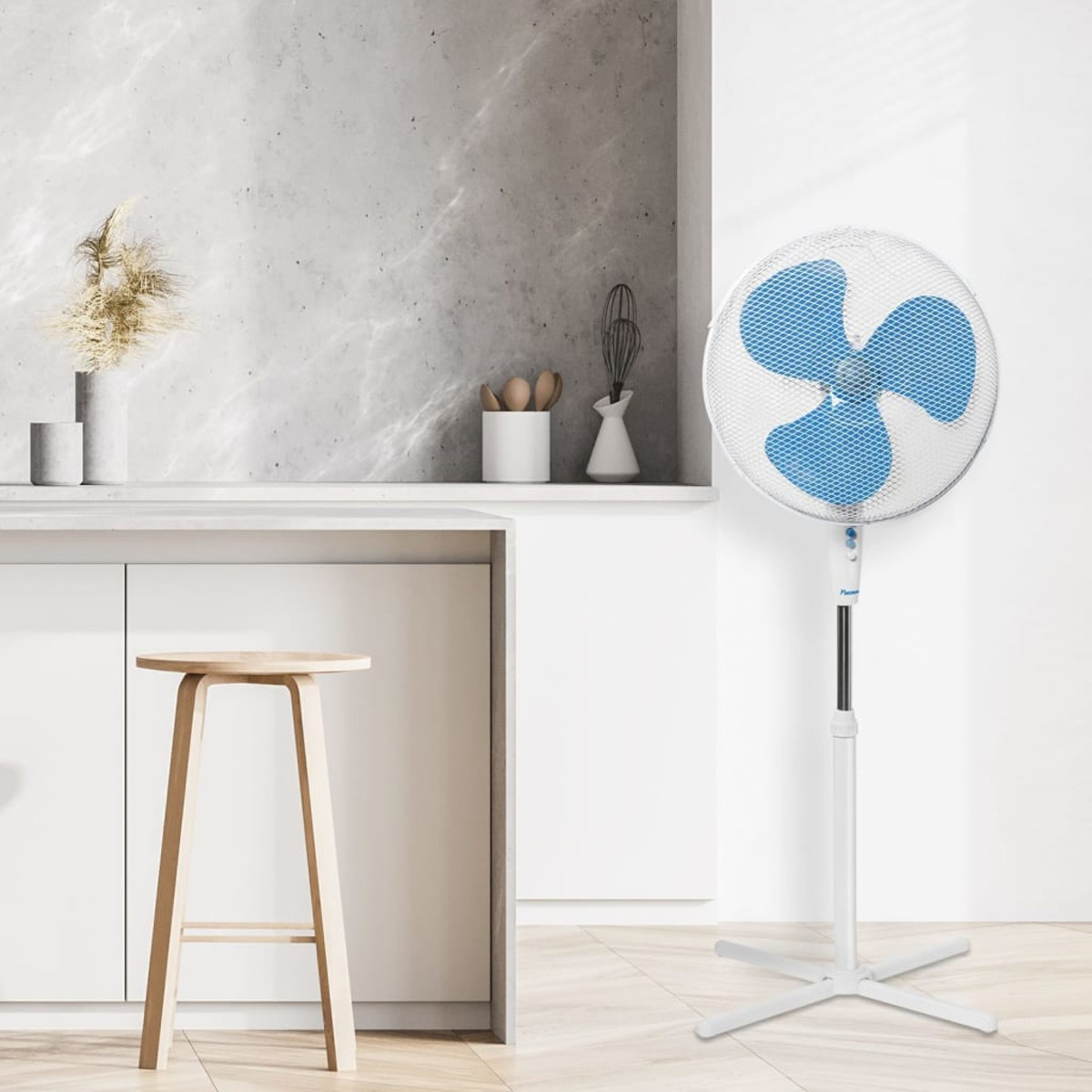 Biały wentylator stojący z niebieskimi łopatkami przed kuchnią.