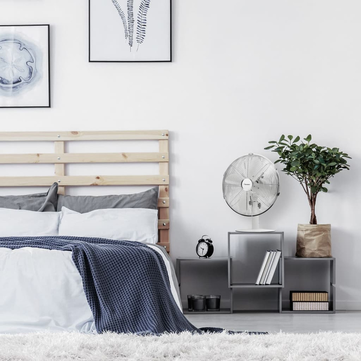 Camera da letto con letto, ventilatore su uno scaffale, piante e opere d'arte sul muro.