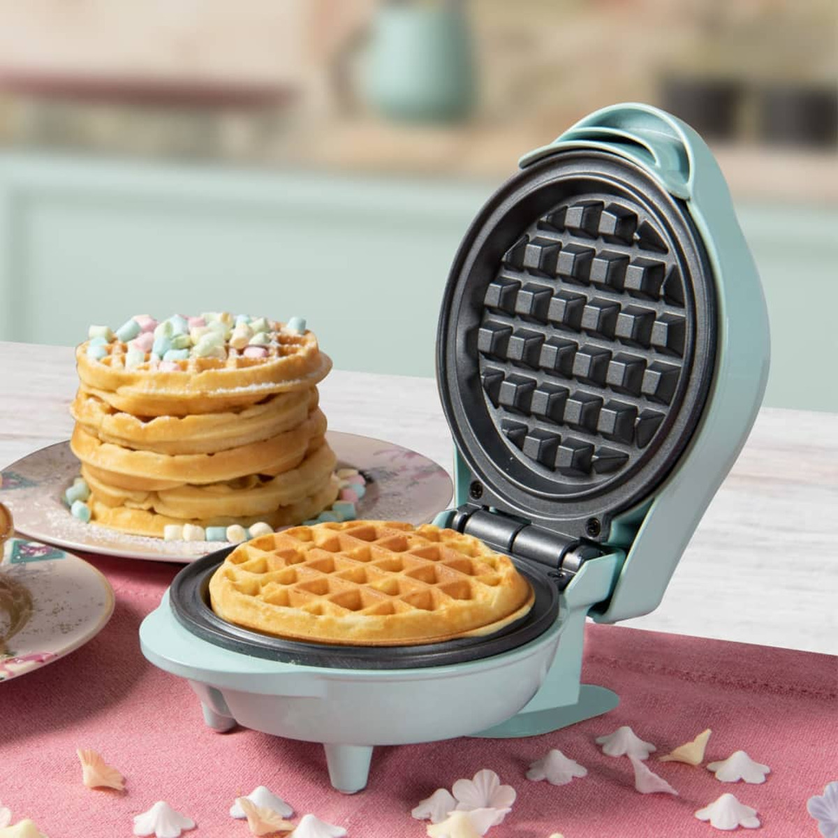 Mini-Waffeleisen mit einer Waffel darin und einem Stapel Waffeln mit Marshmallows.