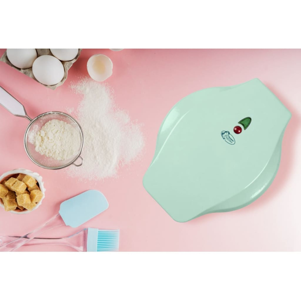 Ein mintgrüner Waffeleisen mit Backzutaten und einer rosa Oberfläche.