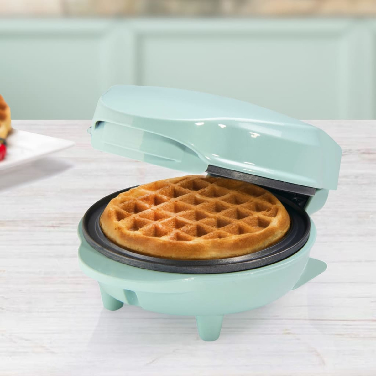 Ein hellblauer Waffeleisen geöffnet, das eine fertige Waffel zeigt, auf einer Holzoberfläche.