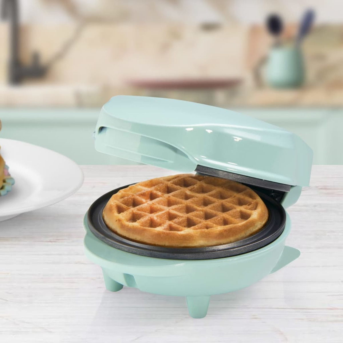 Mintgrüner Waffeleisen mit goldbrauner Waffel darin. Das Waffeleisen ist geöffnet, servierbereit.