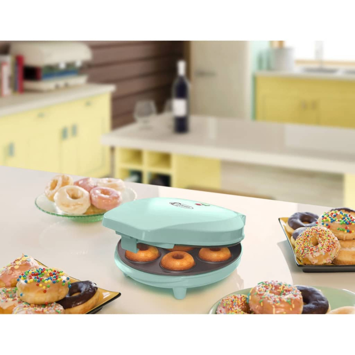 Máquina de hacer donas con donas decoradas en una mesa blanca.