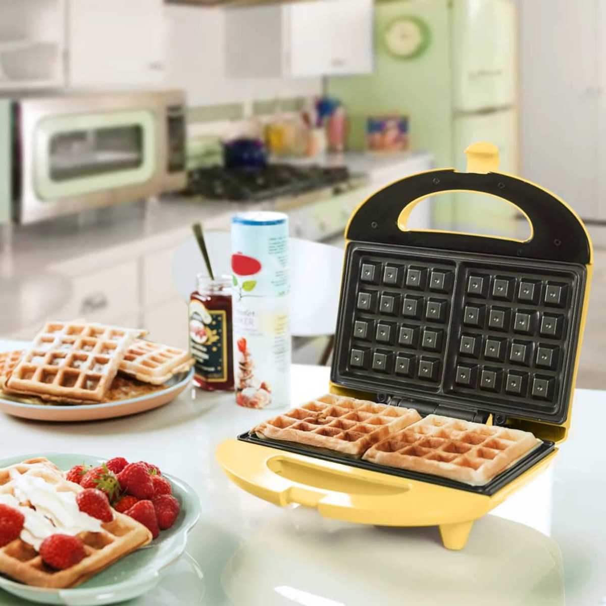Żółta gofrownica z upieczonymi goframi w środku i na talerzu z truskawkami.