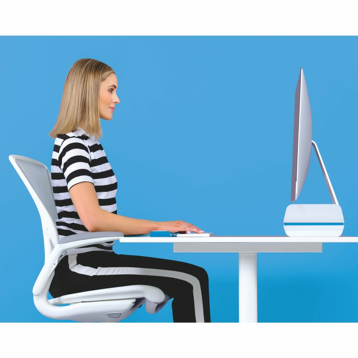 Kobieta siedzi przy biurku, patrzy na ekran komputera, niebieskie tło.