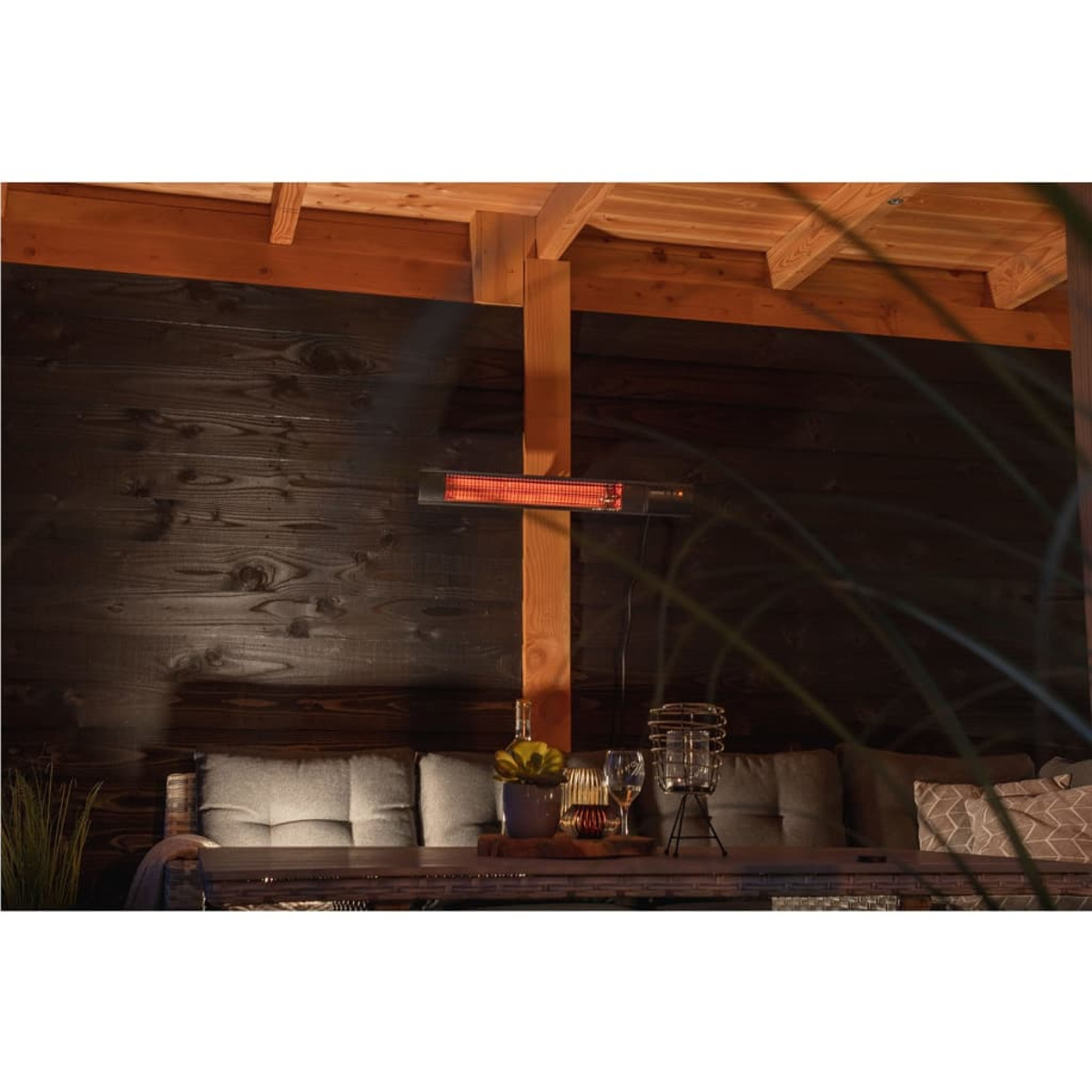 Infraroodverwarming gemonteerd op een houten constructie. Een tafel met glazen, een fles en een kaars eronder.