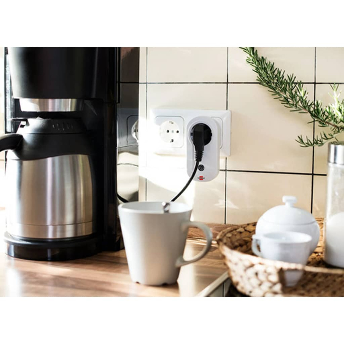 Eine Kaffeemaschine und eine Tasse auf einer Theke. Ein Stecker ist mit einer Steckdose verbunden.