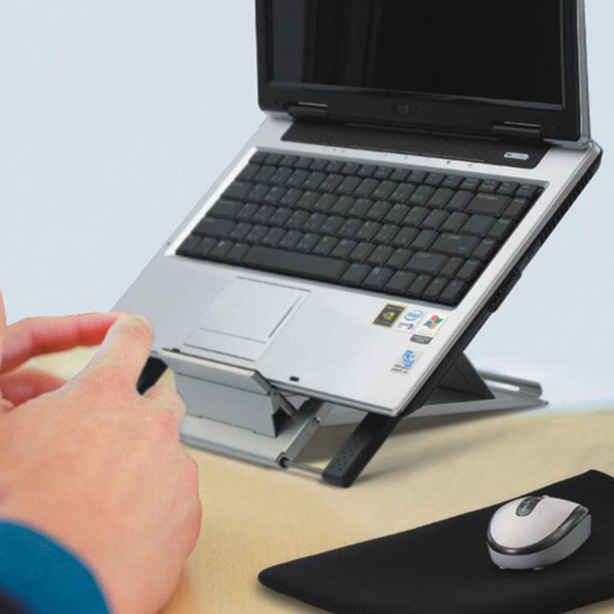 Ein Laptop auf einem Ständer mit Maus und Mauspad. Eine Hand bedient den Laptop.