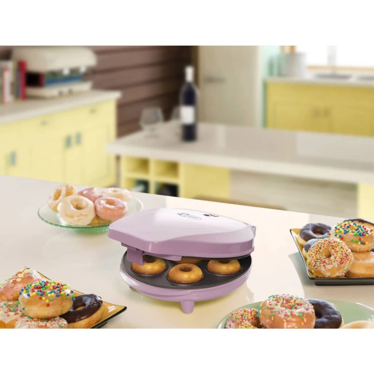Una máquina de hacer donuts morada con donuts en platos, sobre una encimera, con un fondo de cocina borroso.