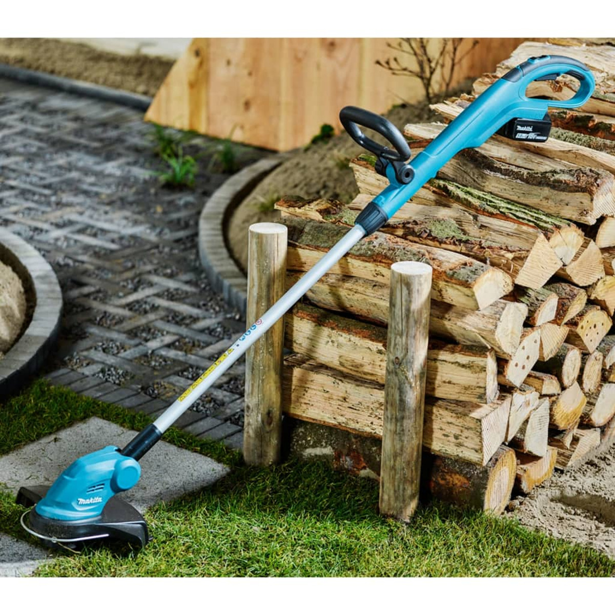 Ein blau-schwarzer Makita-Fadentrimmer neben einem Holzstapel.
