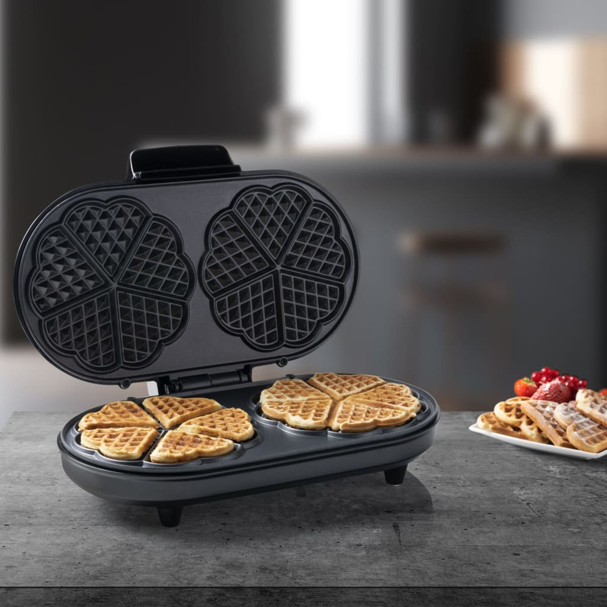 Macchina per waffle con waffle all'interno. Quattro waffle sulla macchina e un piatto con waffle.