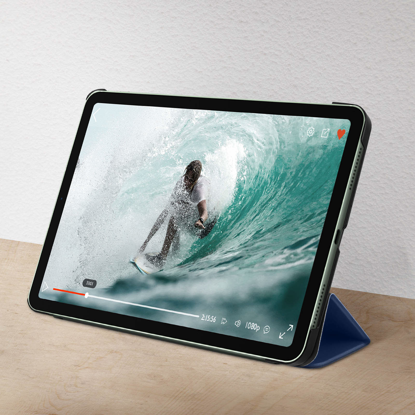 Un iPad mostra un video di surf. La custodia è blu. Lo sfondo è un muro bianco.